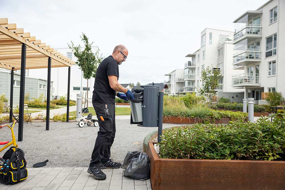 Sidovy av äldre manlig arbetare som placerar grå soptunna i sopställ i bostadsträdgård